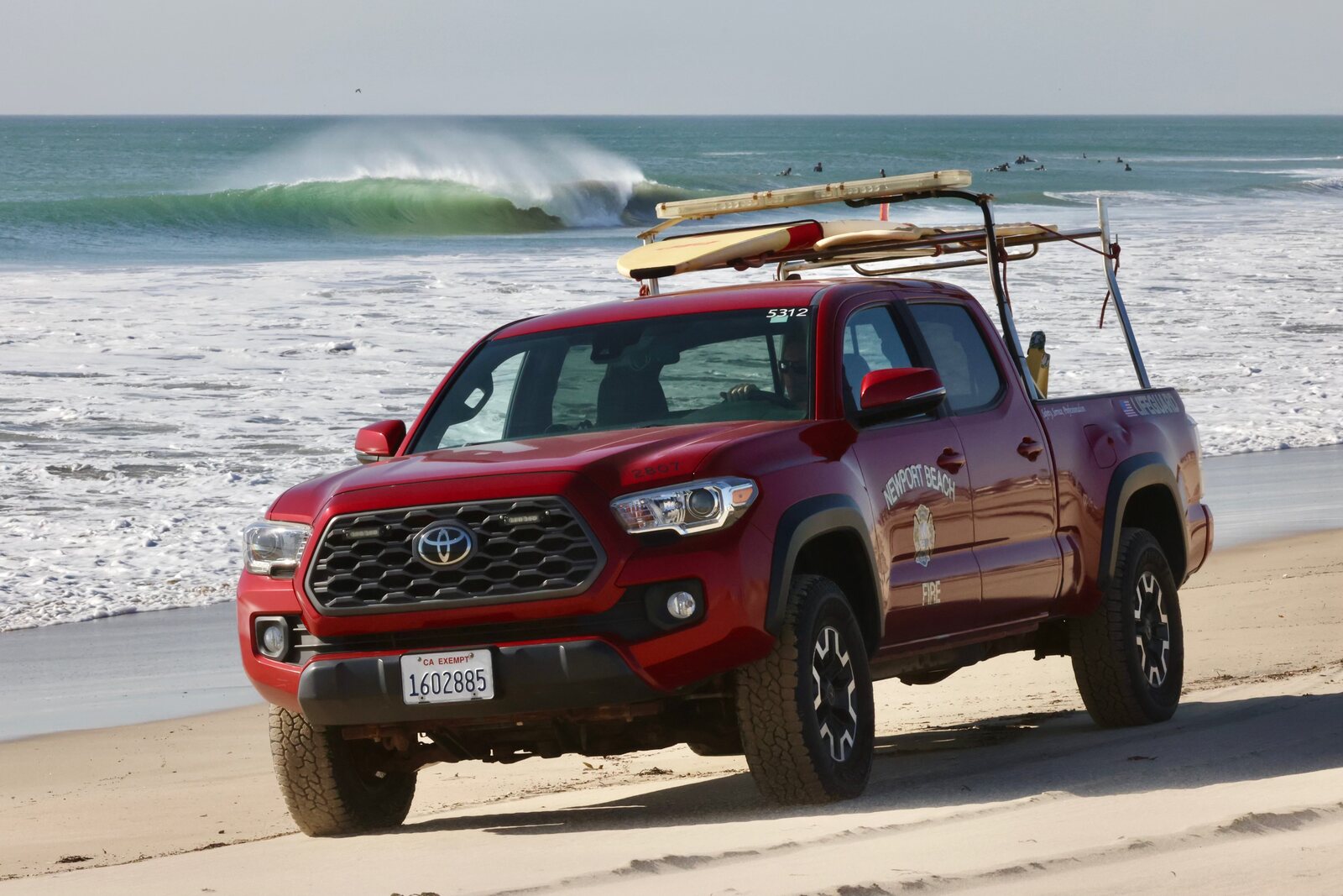 Newport Beach lifeguard truck parked on the sand by the surf.