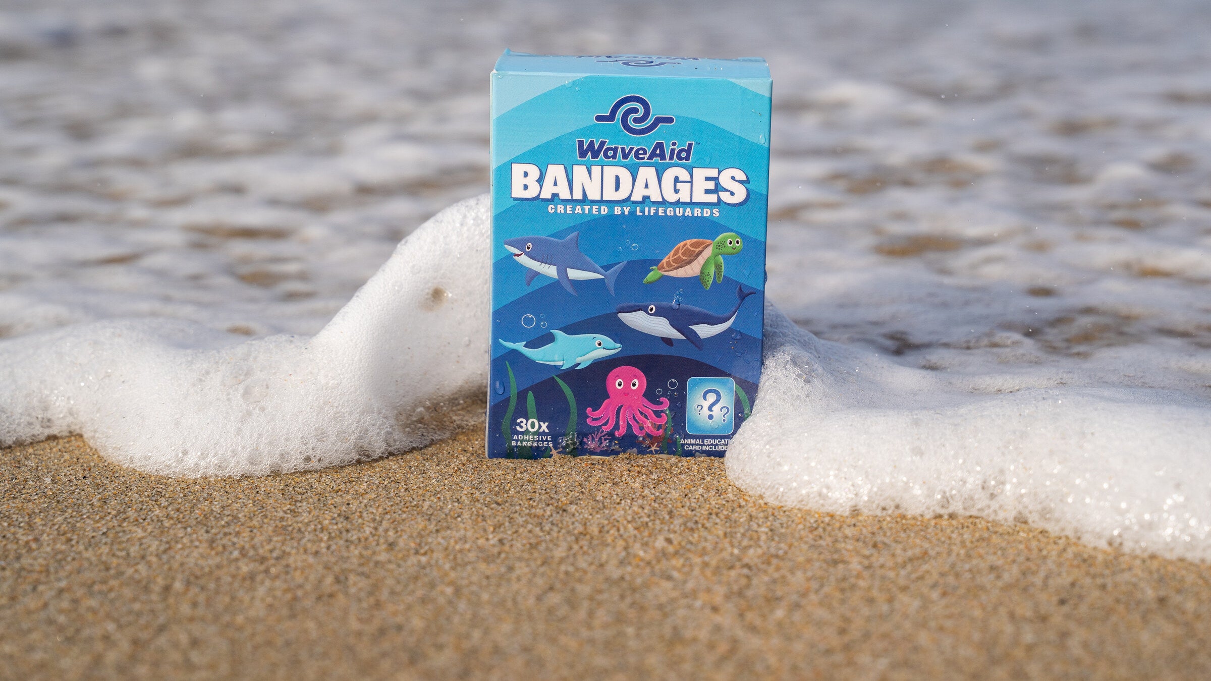 WaveAid bandage box on the sand with surf foam.