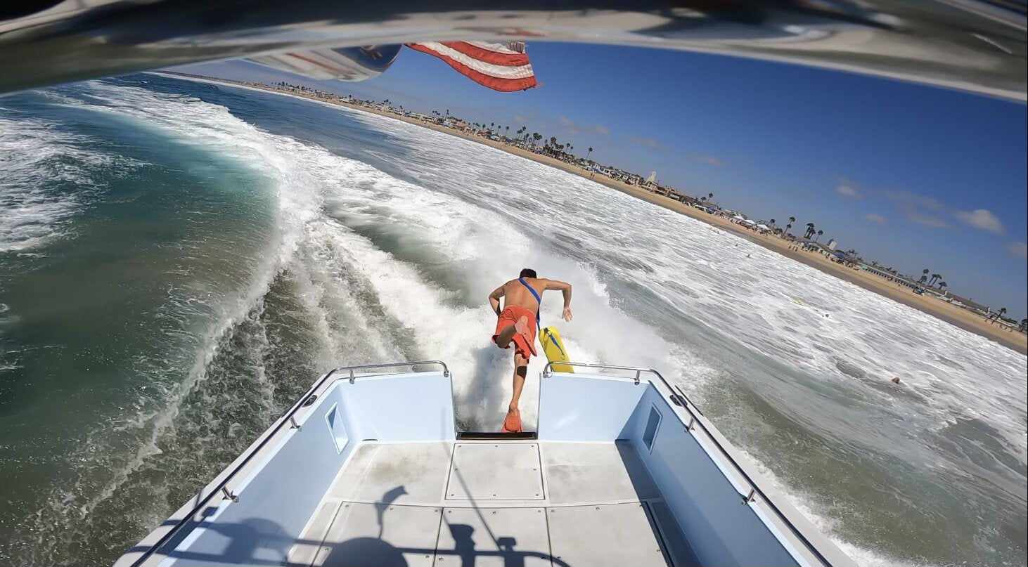 Newport Beach lifeguard launching off the rescue boat with a rescue board.